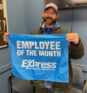 nathan locke smiles at the camera while holding the Employee of the Month banner