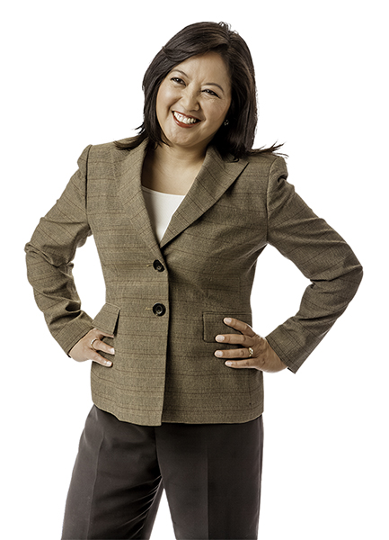 A woman in a brown suit smiling with her hands on her hips.