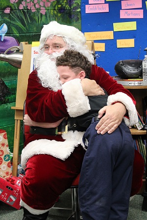 Santa Claus hugging a young kid at a Christmas event.