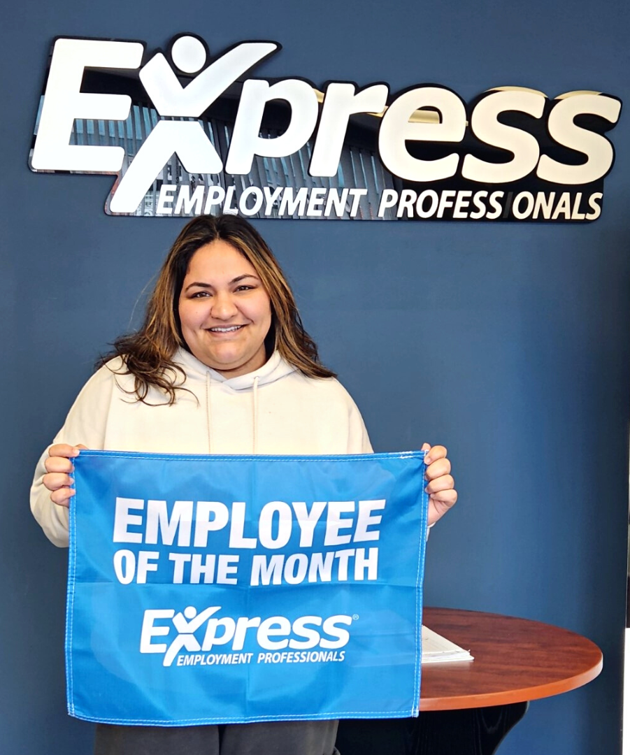 Associate Jalpreet holds an Employee of the Month banner and smiles into the camera