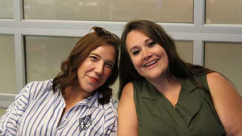 Photo of Marketing Manager wearing blue and white striped dress and Office Manager wearing olive dress. Both women are smiling and enjoying a training session at the franchise group halftime event.
