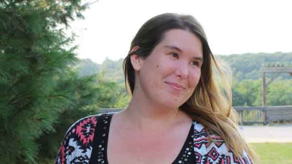 Employment Specialist smiles and looks off into the distance. She is standing outside at a scenic overlook in professional attire.