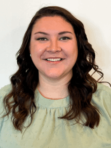 Professional photo of a young woman with curled dark brown hair wearing a mint green short-sleeved blouse