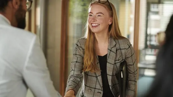 Two people shaking hands in an office setting, with one person holding a folder under their arm.