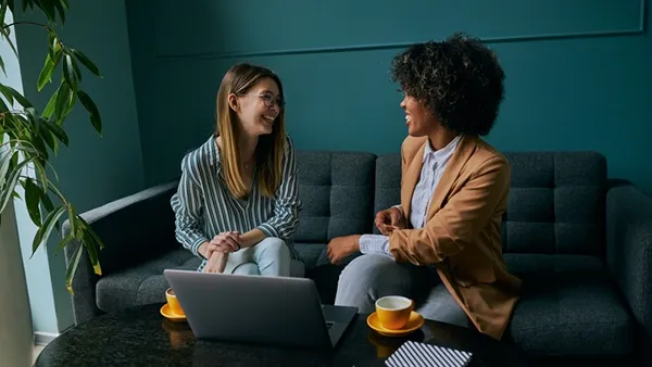 Two young businesswomen are networking in a quiet coffee shop, collaborating over a laptop in a calm, introvert‑friendly setting that supports building referrals without small talk.