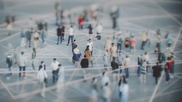 Photo of a blurred crowd of people in varied business-casual clothing standing and walking across a large open space overlaid with interconnected white network lines, representing professional networking or social connections.