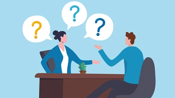 Illustration of two office workers seated across a desk in conversation, with speech bubbles containing question marks above them, symbolizing a discussion, interview, or Q&A session; blue background, brown desk, and small potted plant on the tabletop.