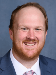 Professional photo of a male with red hair wearing white button-down, blue blazer, and pink tie