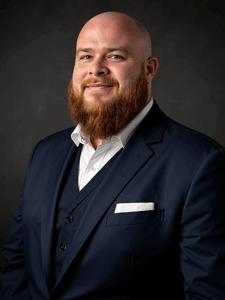 Professional photo of Dylan. He is wearing business professional clothes. He has a red beard..