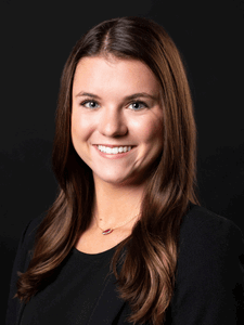 Professional photo of Brenna dressed in professional attire. Brenna is a young woman with dark hair. 